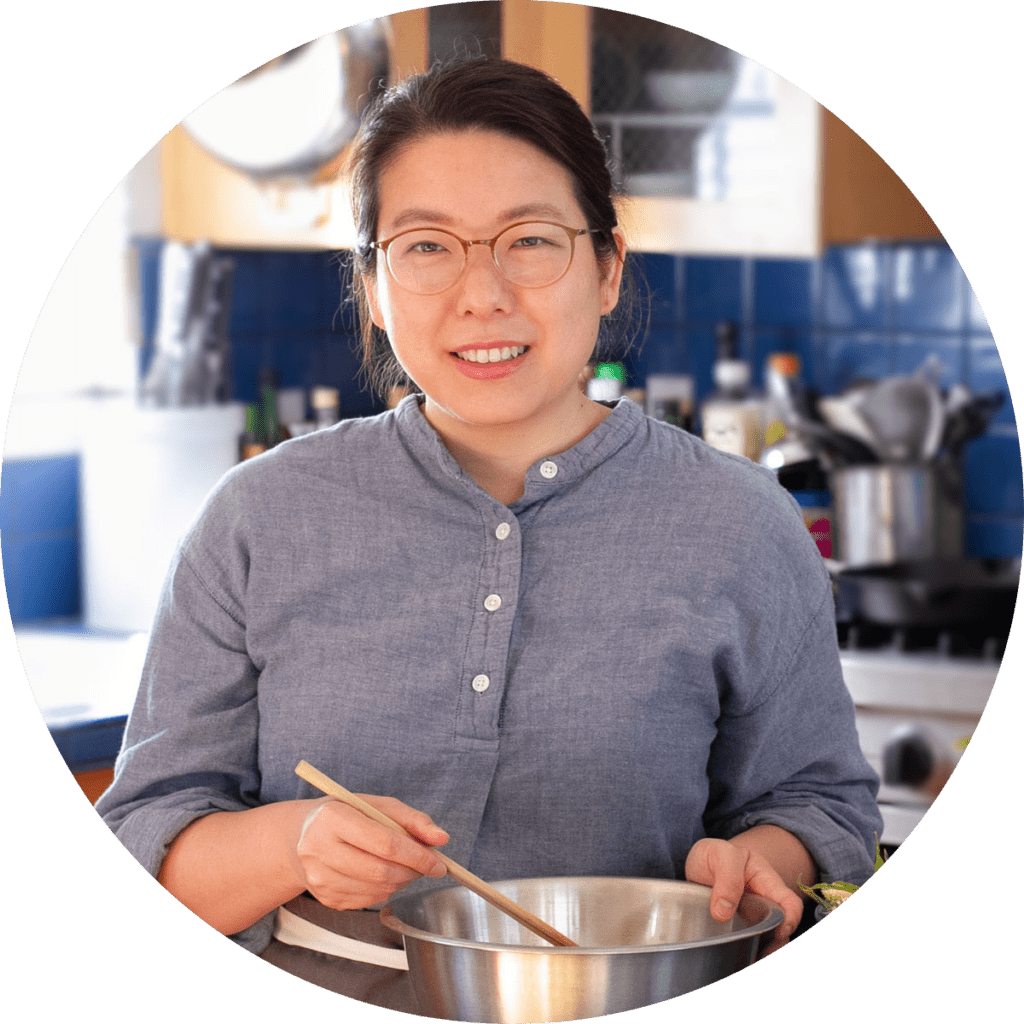 Cindy standing in a kitchen and smiling, mixing food in metal bowl with chopsticks.