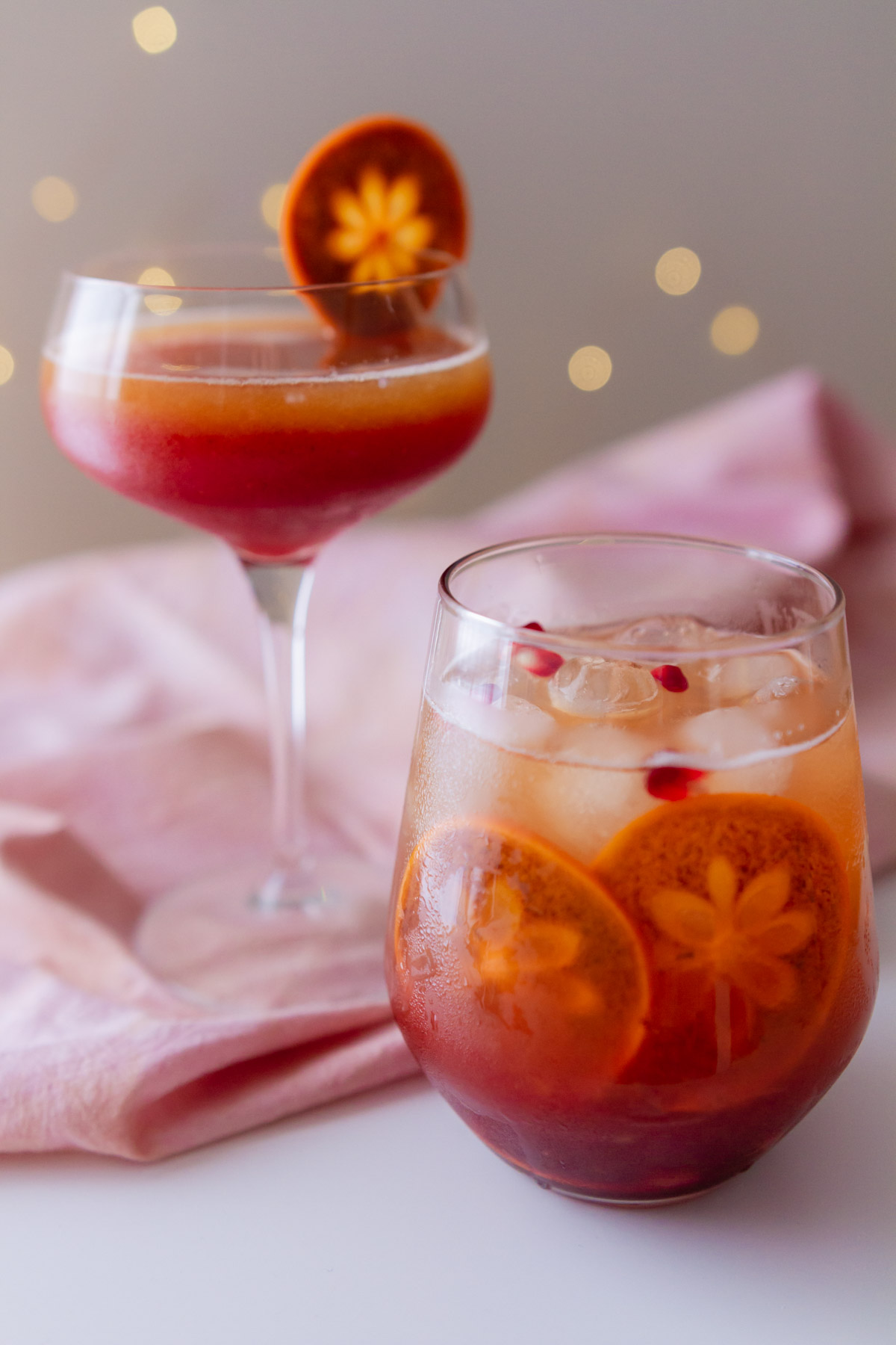 Sparkling pomegranate mocktail served in two different glasses with ice, slices of fuyu persimmon, and pomegranate arils.