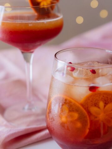 Sparkling pomegranate mocktail served in two different glasses with ice, slices of fuyu persimmon, and pomegranate arils.
